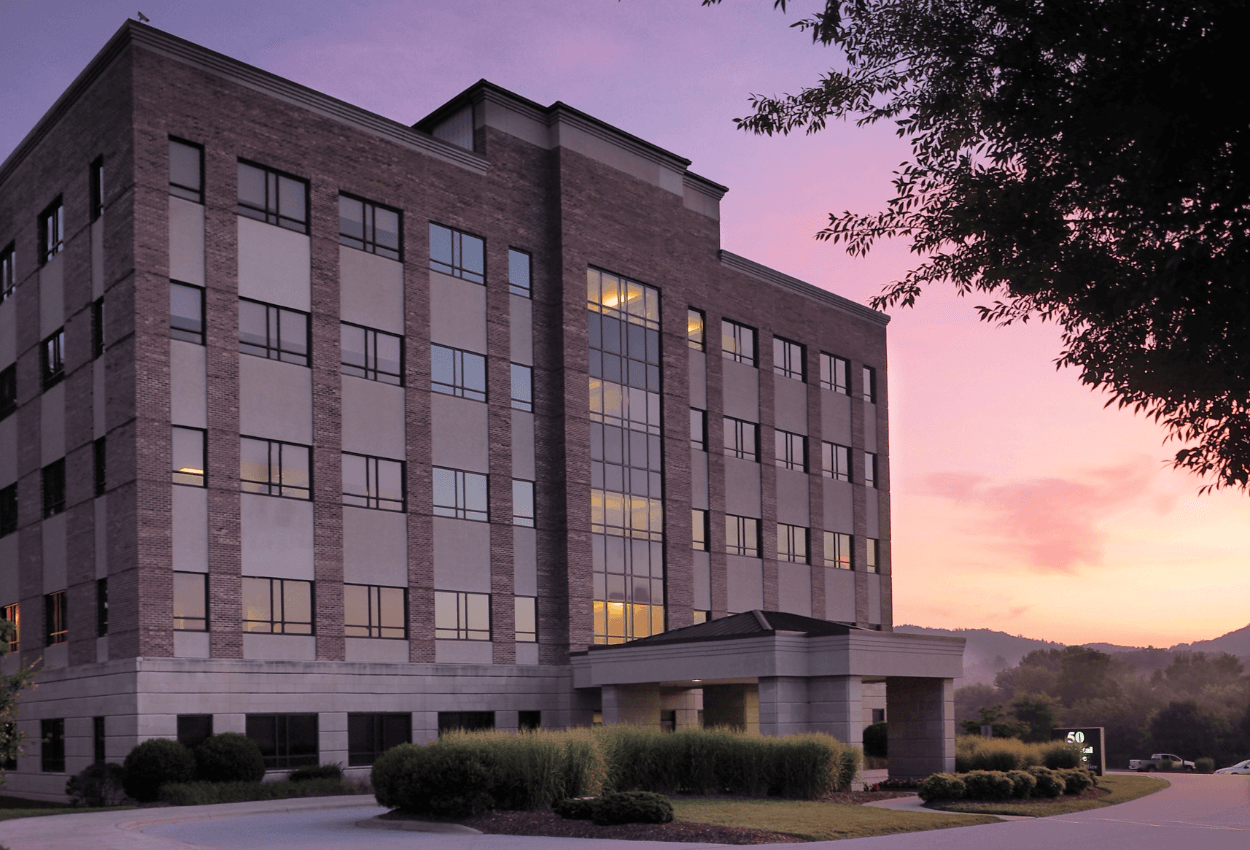 The image shows a large medical building, and in the background is a yellow and purple sunset.